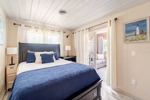 A bedroom with a bed, nightstands, a lamp, a painting, and a view through an open door. - Ripple Inn: private retreat mins to the Gulf (South Venice)