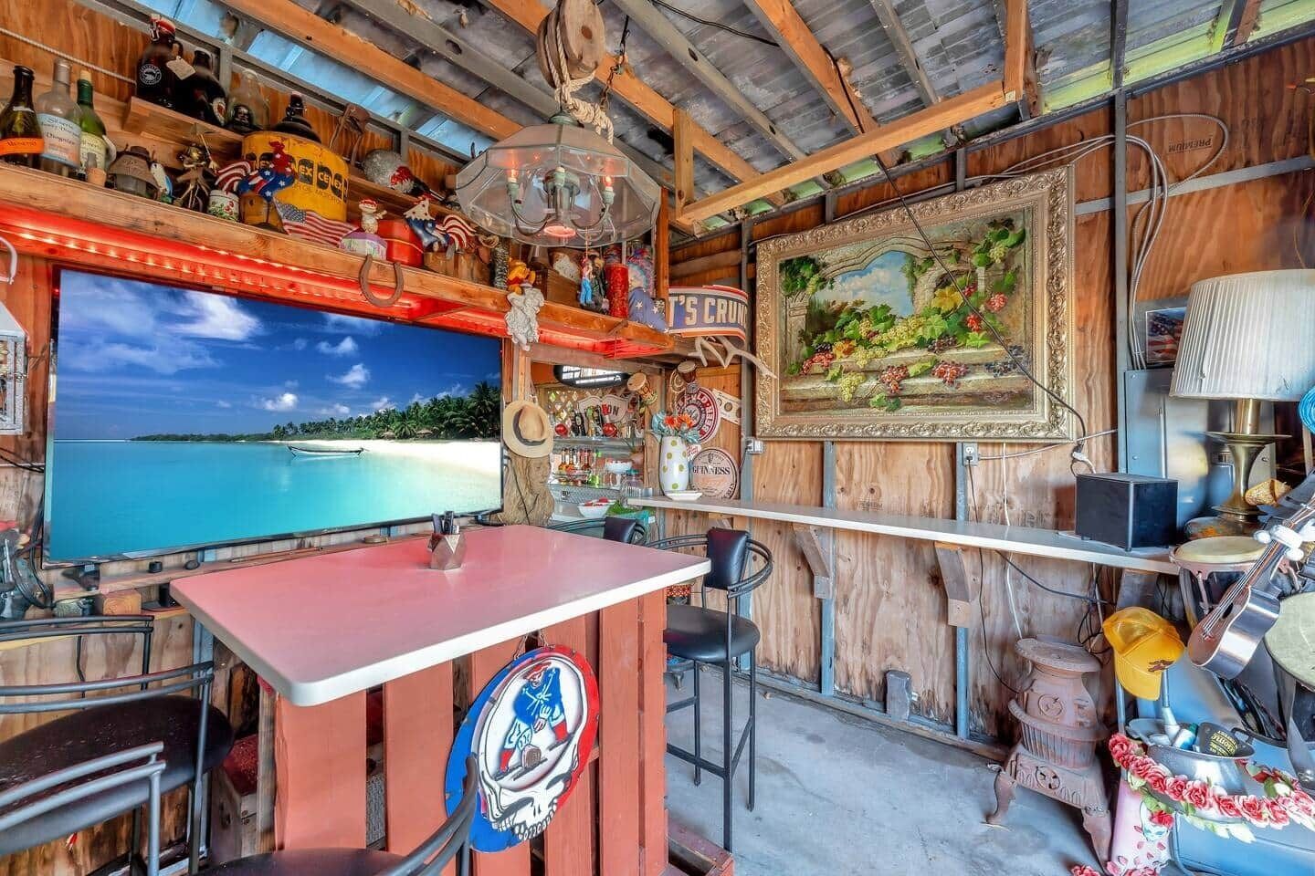 Een barruimte met een televisie waarop een uitzicht op het strand te zien is, houten wanden en diverse decoraties.