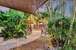 A pathway leading to a building with a covered entrance, surrounded by lush tropical plants and a decorative wheel. - Daze Inn Between: lagoon pool mins to beaches (South Venice)