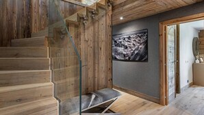 Una escalera de madera con barandillas de vidrio y un banco, una fotografía enmarcada en la pared, y un techo de madera.