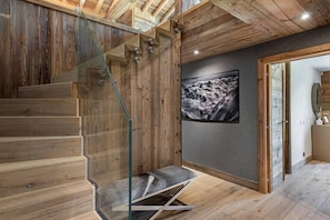 Eine Holztreppe mit Glastrennfeldern und einer Bank, ein gerahmtes Foto an der Wand und eine Holzbalkendecke.
