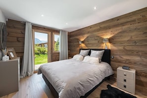 Ein Schlafzimmer mit einer Holzwand, einem Bett mit weißer Bettwäsche, einem Nachttisch und Blick auf Grünfläche draußen.