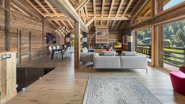 Un interior moderno con vigas de madera, un sofá, una zona de comedor y ventanas amplias.