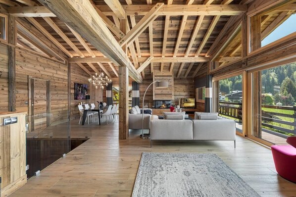 Ein modernes Interieur mit Holzbalken, einer Couch, einem Essbereich und großen Fenstern.