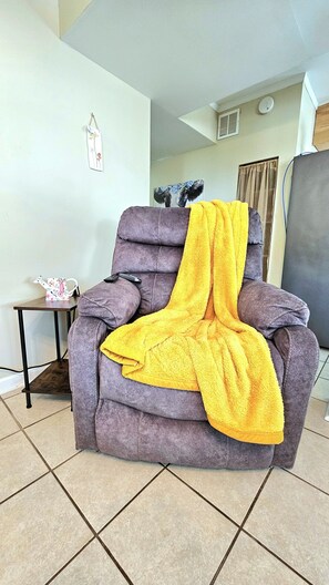 Ein graues Sofa mit einer gelben Decke, ein kleiner Tisch mit einem dekorativen Gegenstand und ein Bild an der Wand.
