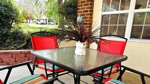 Un patio al aire libre con una mesa de vidrio, sillas rojas con cojines a rayas y una figurita de animal de cerámica blanca.