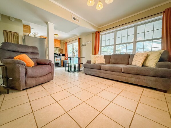 A spacious living room with two sofas, a dining table, and a kitchen in the background.