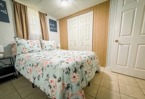 A bedroom with a bed, a nightstand, a lamp, a door, and a wall with a sign. -  Unique Stay- Meet our pet Goat Mila- Near 
I-75 & Shops - Pet Friendly (Cleveland)