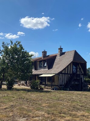 Une maison traditionnelle à colombages, avec un toit à forte pente, une cheminée et un petit porche.