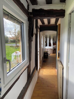 Un couloir étroit avec des poutres en bois apparentes, une fenêtre et une vue sur un jardin extérieur.