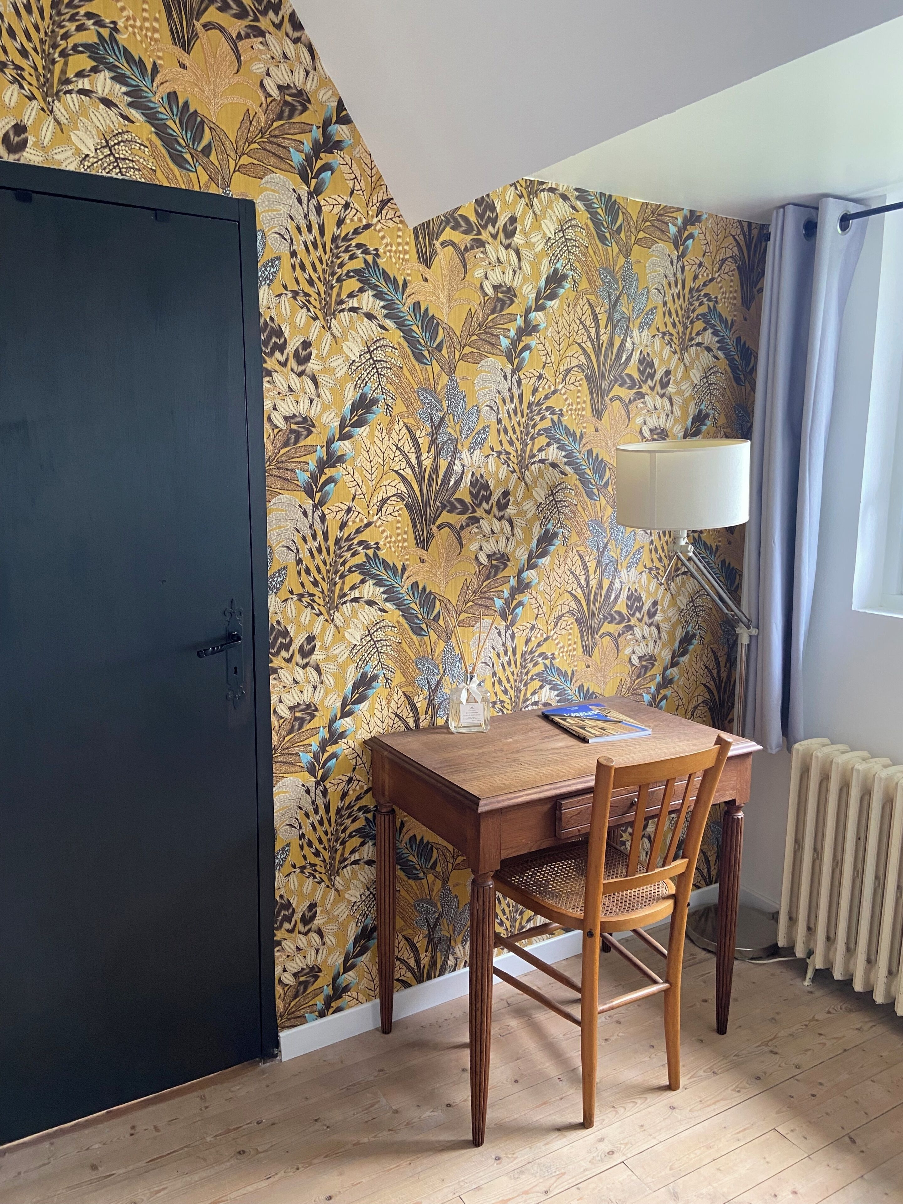 Une pièce avec une porte sombre, une table avec une lampe et un papier peint à motifs.