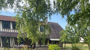 Une table ronde d’extérieur, entourée de chaises, se trouve au milieu d’un jardin, avec une maison en arrière-plan.