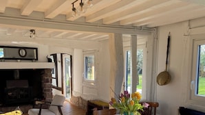 Une pièce avec une cheminée, des meubles en bois, une table à manger recouverte d’une nappe à motifs floraux et une vue sur l’extérieur.