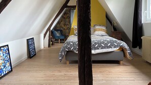 Une chambre mansardée avec un plafond en pente, un lit avec une literie à motifs, un plancher en bois et deux œuvres d’art encadrées accrochées au mur.