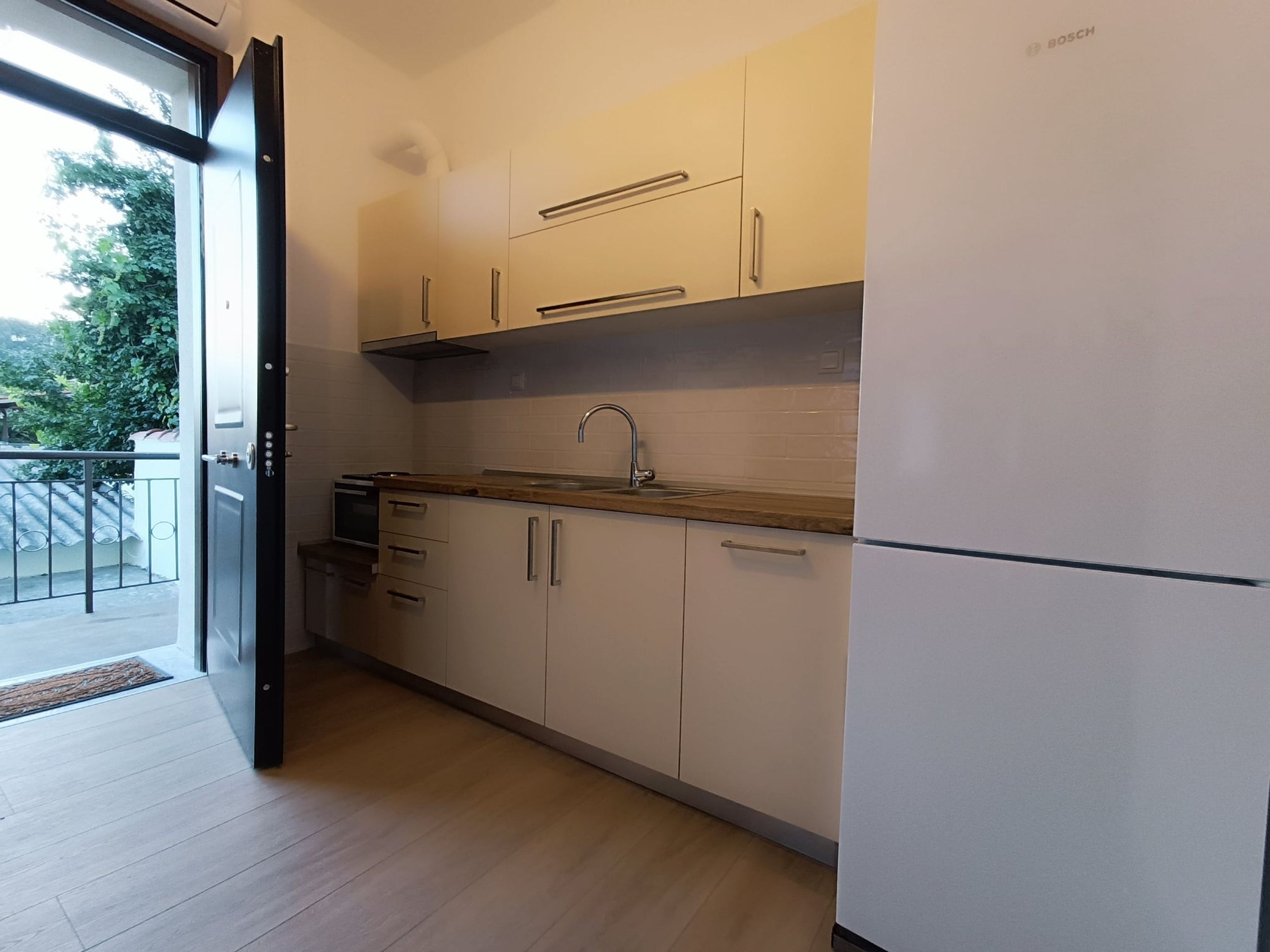 Une cuisine moderne avec des meubles blancs, un évier en acier inoxydable et un réfrigérateur de la marque Bosch.