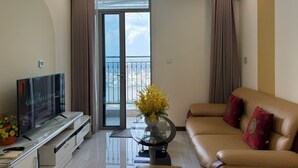 Ein Wohnzimmer mit einer Couch, einem Fernseher, einem Couchtisch und einem Balkon mit Vorhängen.
