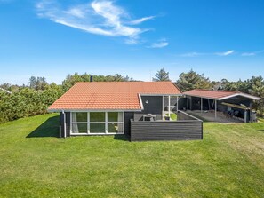 Une maison moderne avec un toit recouvert de tuiles rouges, un patio abrité et une pelouse bien entretenue.