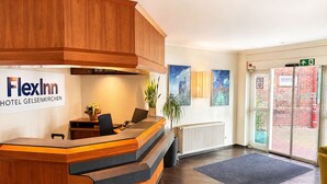 A hotel reception desk with a sign for FlexInn Hotel Gelsenkirchen, a plant, and artwork on the wall.