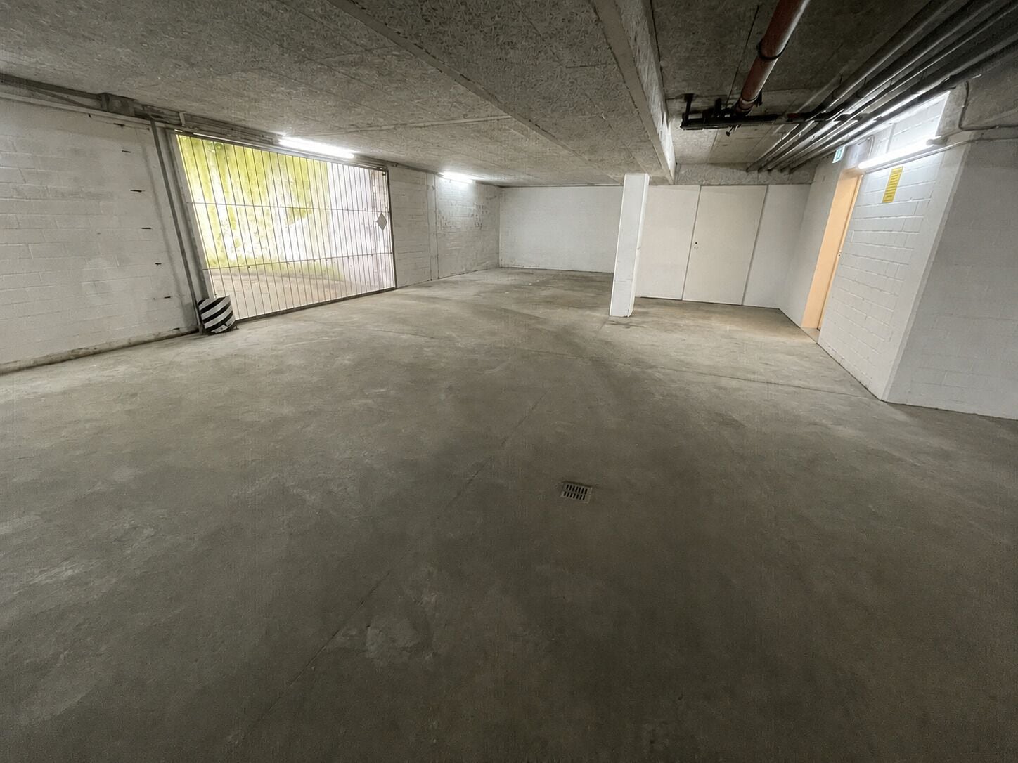 A spacious underground parking area with concrete floors and walls, a metal gate, and a vent on the ceiling.