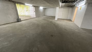 A spacious underground parking area with concrete floors and walls, a metal gate, and a vent on the ceiling.