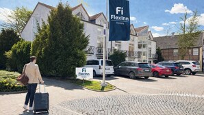 A hotel entrance with a sign for FlexInn Hotels, a person with a suitcase, and parked cars.