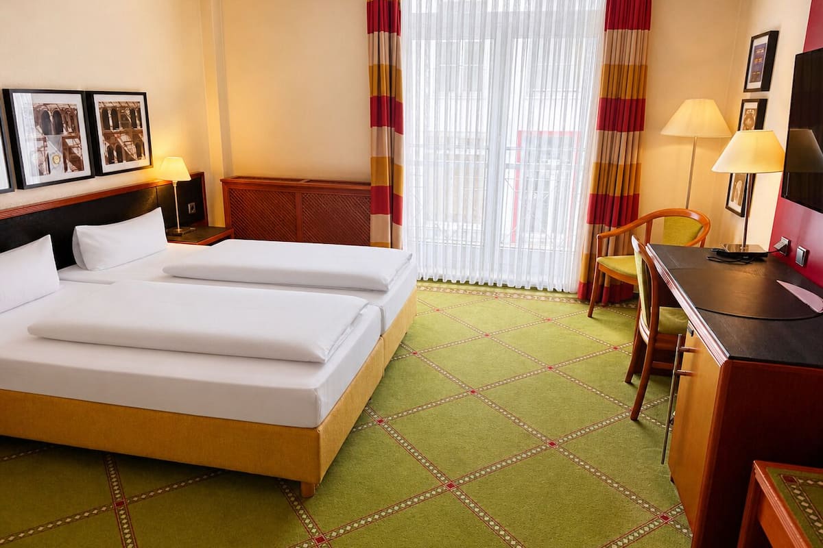 A hotel room with two beds, a desk, a chair, a TV, and a window with curtains.