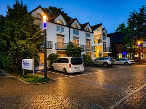 A hotel with a signboard, a paved parking area, and a building with multiple windows and balconies.