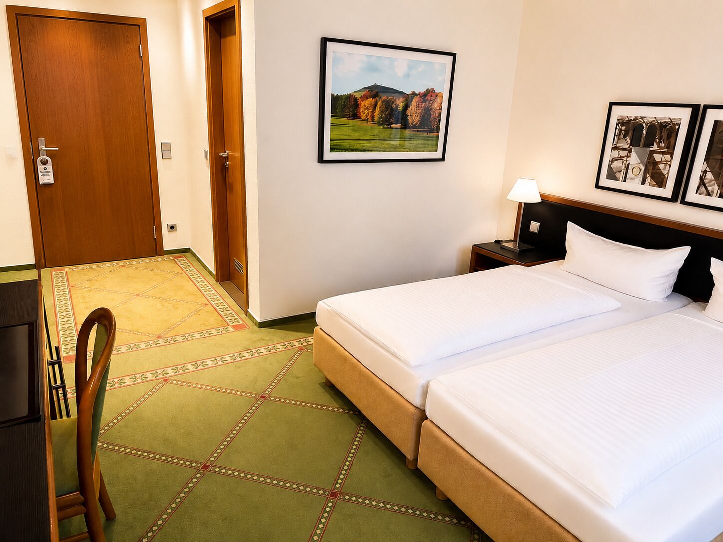 A hotel room with a bed, a desk, a chair, a picture on the wall, and a carpet.