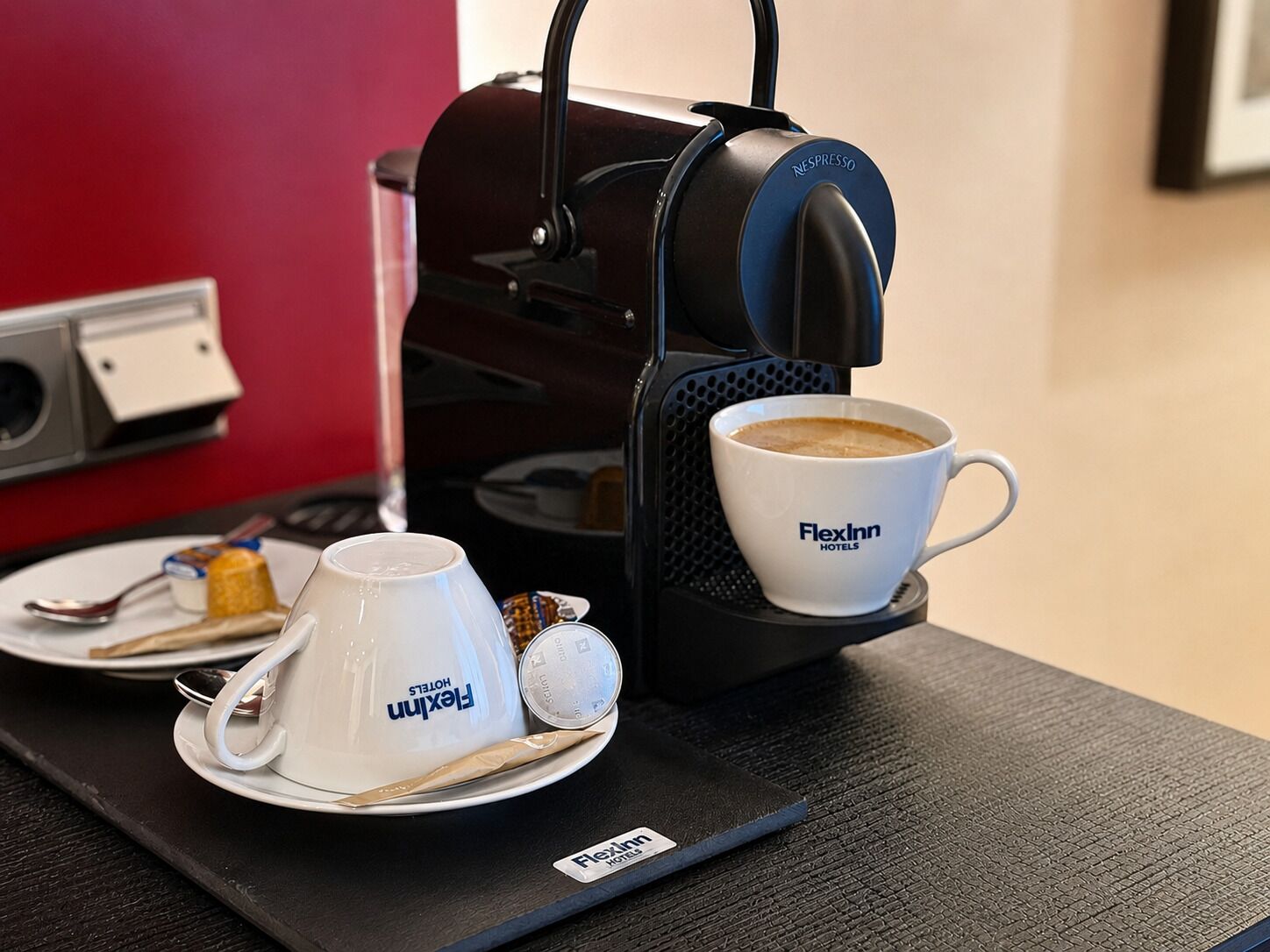 A FlexInn hotel coffee station with a Nespresso machine, a cup of coffee, and a FlexInn branded cup.