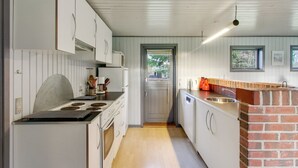 Ett kompakt kök med vita skåp, en tegelvägg som accent, en inbyggd ugn och en diskho.