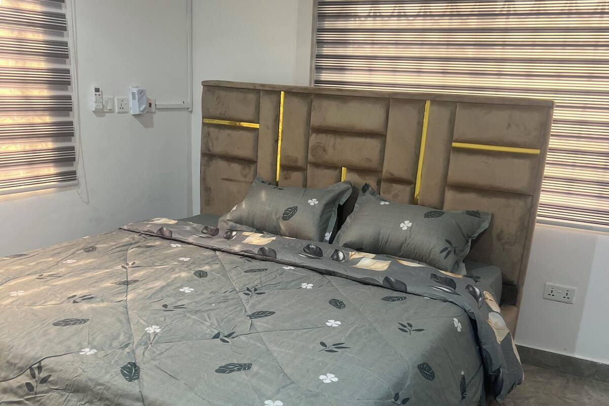 A bedroom with a bed, headboard, and window blinds.
