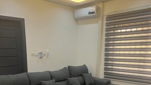 A sectional sofa in a room with a marble-patterned floor, an air conditioning unit, and a patterned wall. - CANA Unique Flats (Kwabenya)