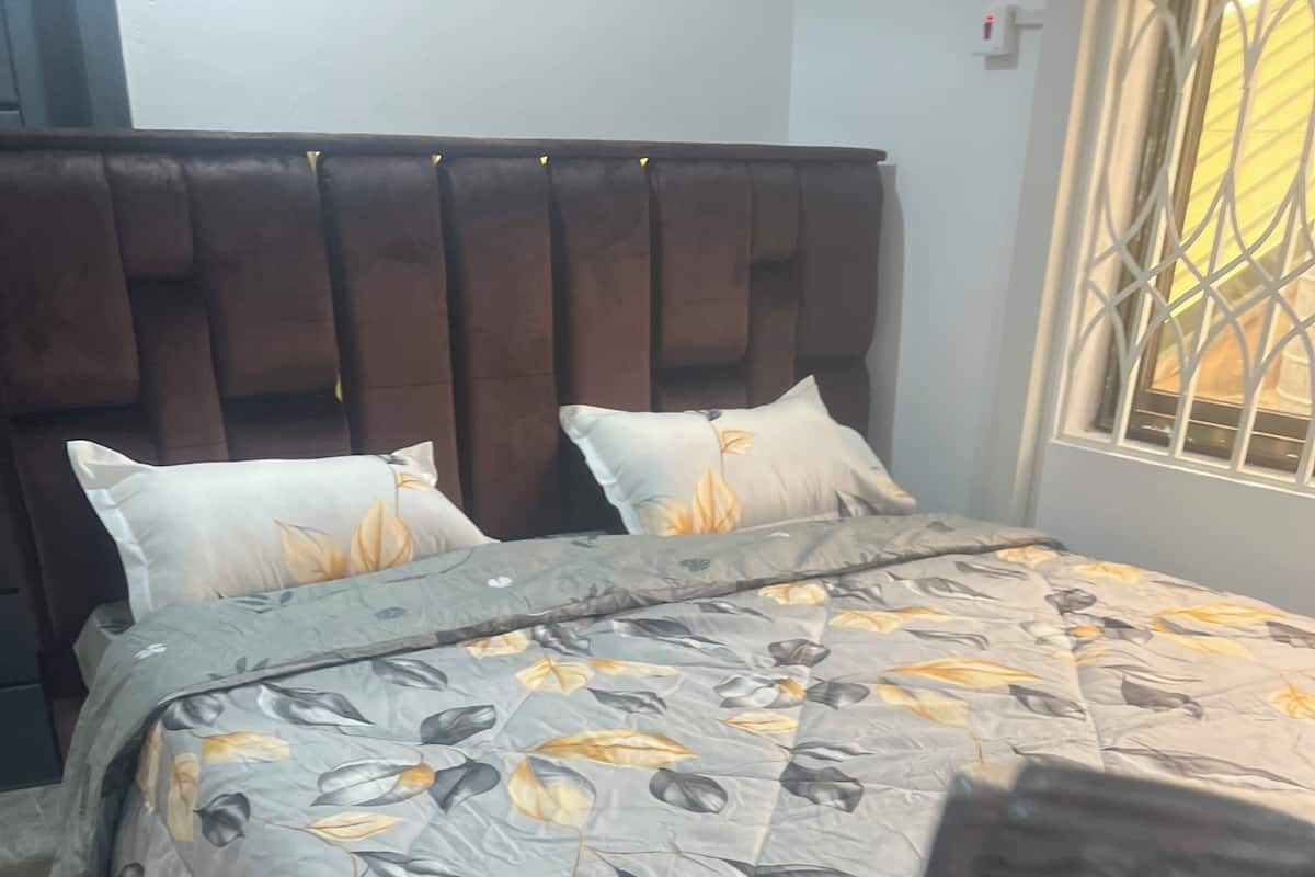 A bed with a leaf-patterned bedspread, a dark headboard, and a window with a metal grille.