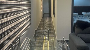 A hallway with a glass table, metal chairs, a sofa, and a bed in the background. - CANA Unique Flats (Kwabenya)