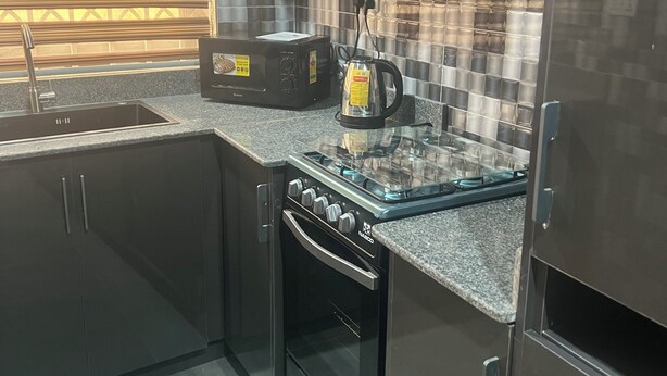 A modern kitchen with a built-in oven, a microwave, and a kettle on the countertop. - CANA Unique Flats (Kwabenya)