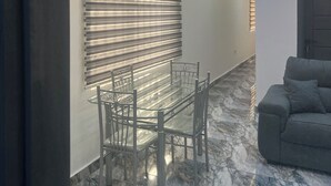 A modern interior with a dining area featuring a glass table and chairs, a sofa, and a wall with a patterned blind. - CANA Unique Flats (Kwabenya)