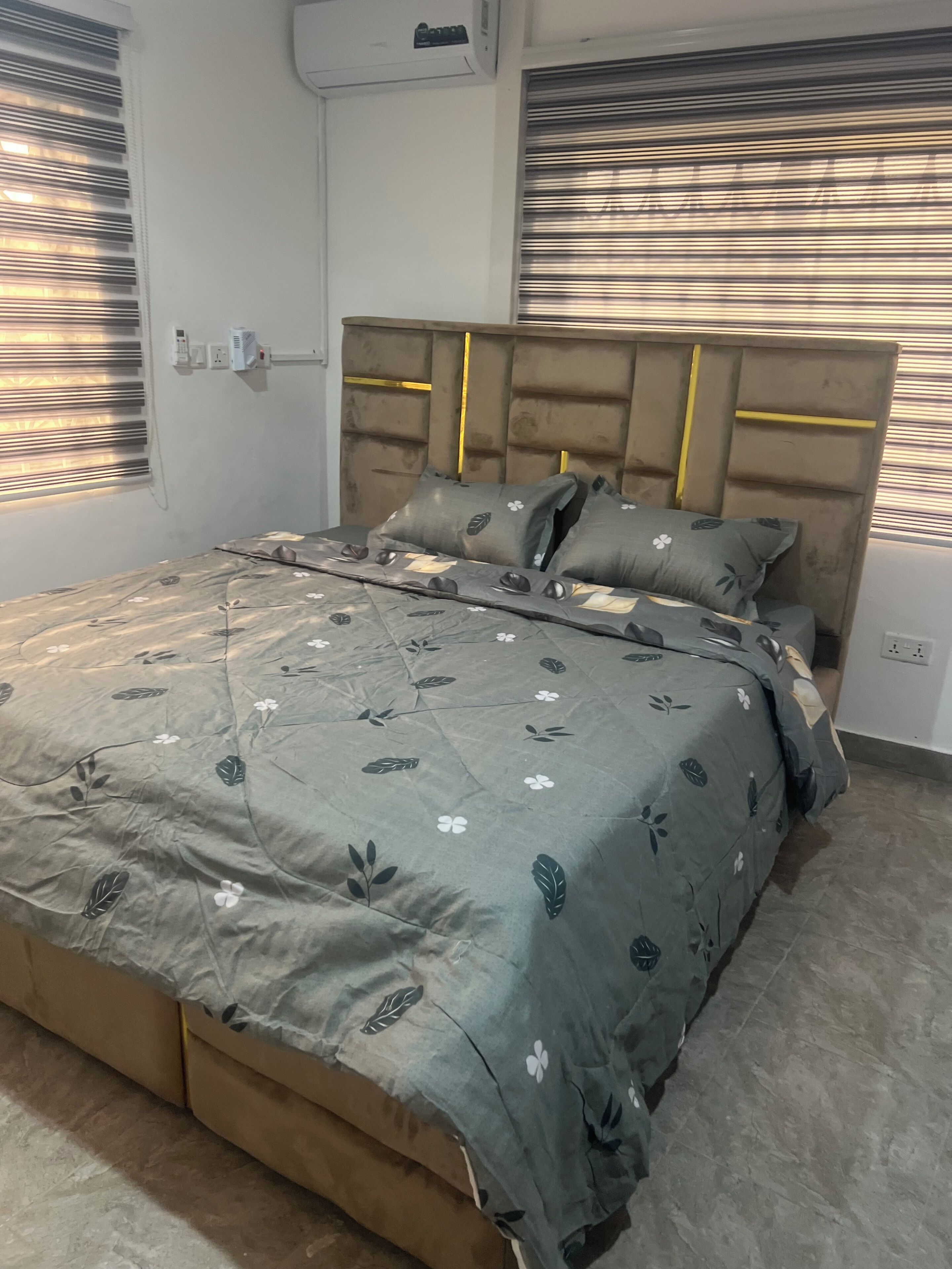 Un dormitorio con cama, cabecera, ventana y aire acondicionado instalado en la pared.