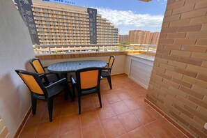 A balcony with a round table and four chairs, a brick wall, and a view of a hotel building. - ACV - Aguamarina-2ª linea planta 4 sur (OROPESA)