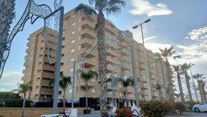 Um edifício com vários andares e varandas, rodeado por palmeiras e postes de luz.
