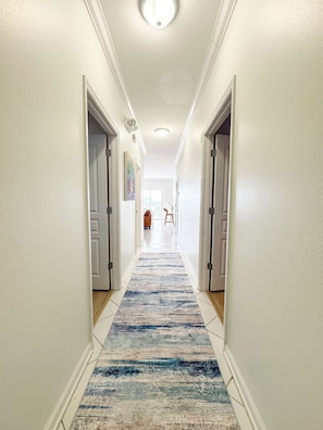 A hallway with a patterned carpet, white walls, and doors on either side. - Destin Harbor Escape (Destin)