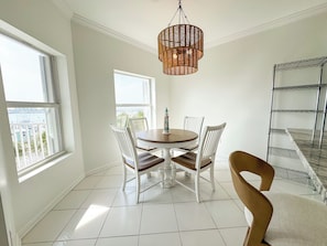 A dining area with a round table, white chairs, a hanging light fixture, and a view of the sea through large windows. - Destin Harbor Escape (Destin)