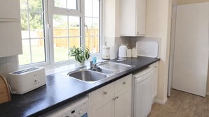A kitchen with a double sink, a toaster, a dishwasher, and a window with a view of a wooden fence.