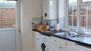 A compact kitchen with a washing machine, a built-in oven, a sink, and a window with a view of the outside.