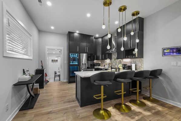 A modern kitchen with a central island, black bar stools, and a built-in oven.