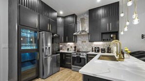 A modern kitchen with dark cabinets, stainless steel appliances, and a marble countertop. - New Indy Game House- Theater + Arcade - Sleeps 12 (Indianapolis)