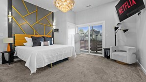 A bedroom with a bed, a chandelier, a TV, and a view of the outside. - New Indy Game House- Theater + Arcade - Sleeps 12 (Indianapolis)