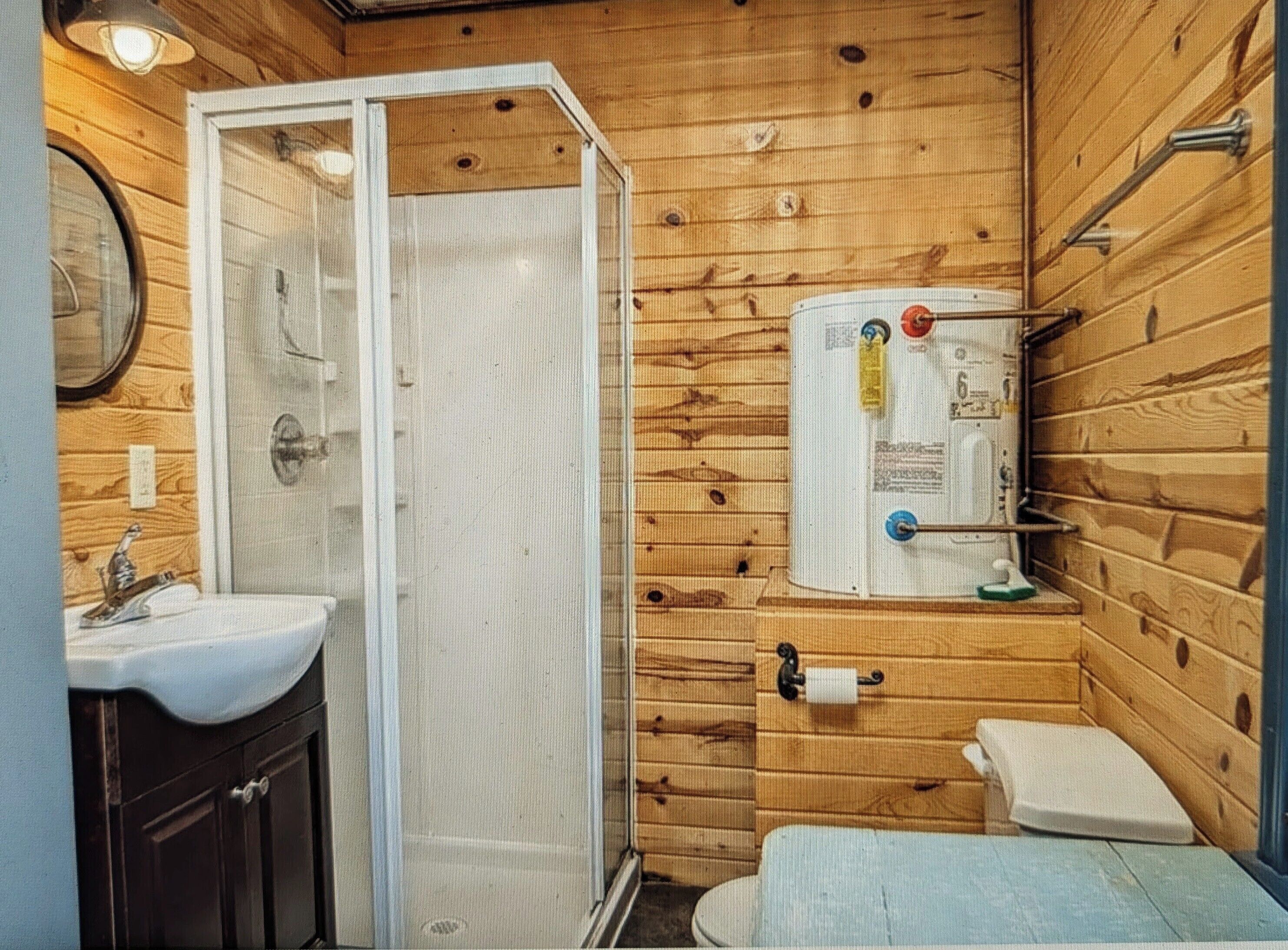 A compact bathroom with a shower, toilet, sink, and a water heater mounted on the wall.