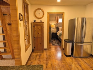 A wooden staircase leading to a bedroom with a bed, a refrigerator, and a clock on the wall.