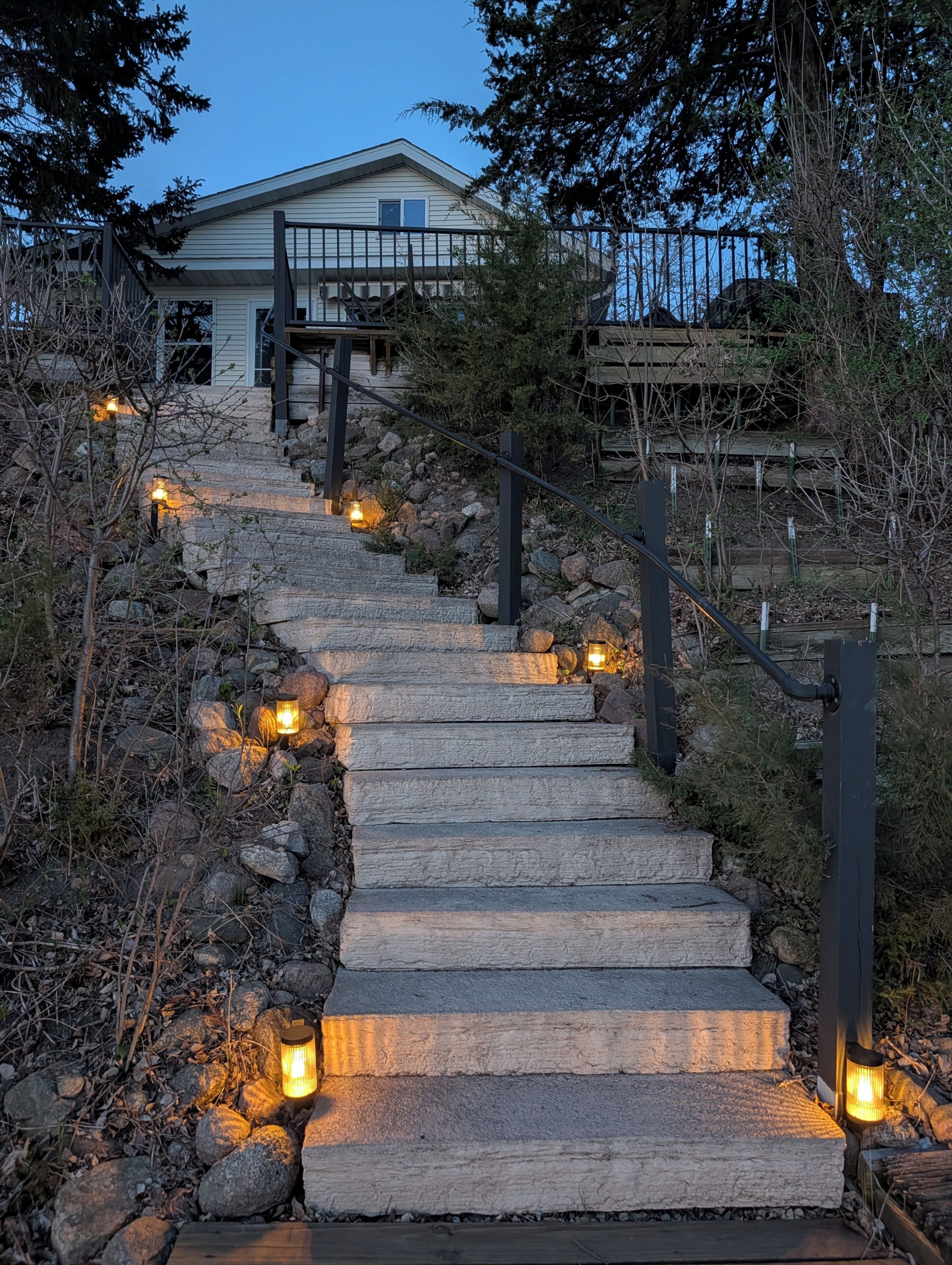 A stone staircase leading to a house with a wooden deck, surrounded by trees and rocks.