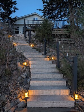 A stone staircase leading to a house with a wooden deck, surrounded by trees and rocks.